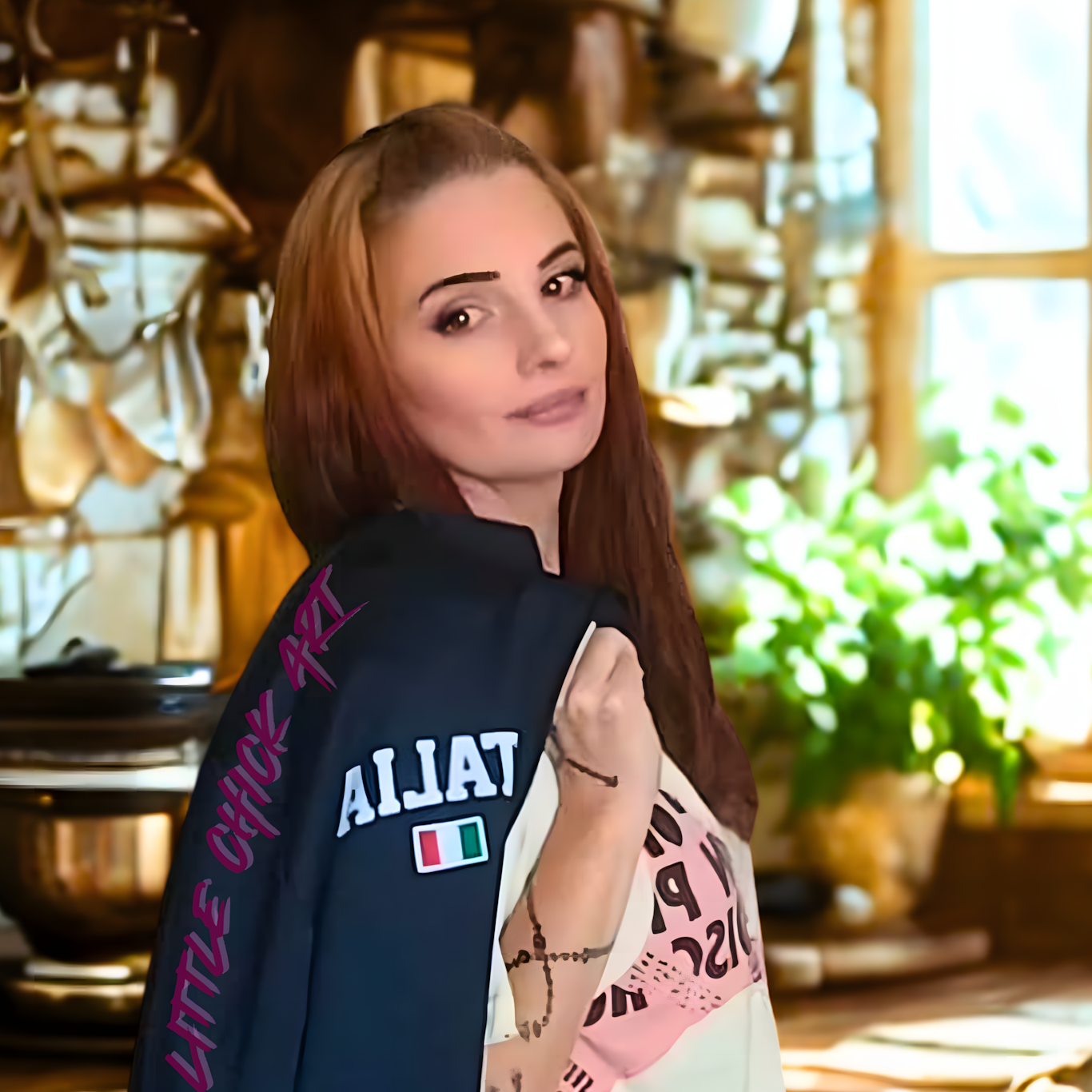 Woman standing in a kitchen holding a navy blue jacket with colorful text and graphics.